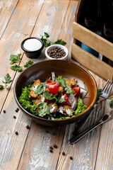 A vibrant salad featuring grilled chicken, fresh greens, tomatoes, and cilantro is beautifully arranged on a wooden table. Accompanied by seasonings, it invites a wholesome dining experience