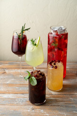 Colorful drinks filled with fruits and herbs sit on a wooden table, perfect for a summer gathering. Each glass showcases unique colors and refreshing ingredients, inviting relaxation