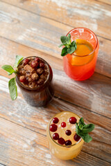 Three vibrant cocktails sit atop a rustic wooden table, adorned with fresh mint and garnished with berries. Perfect for a warm summer day and enjoyable with friends