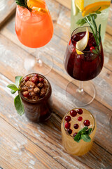 A variety of vibrant cocktails sit on a weathered wooden table, each adorned with fruits and herbs, perfect for a warm, festive afternoon among friends