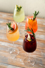 Four vibrant cocktails are displayed on a rustic wooden table, each garnished with fresh herbs and fruit. The sunlight softly highlights their colors, creating an inviting atmosphere