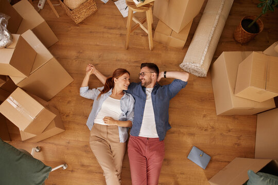 A couple relaxes on the floor, smiling at each other while surrounded by cardboard boxes in their new home. They have just completed a day of moving and organizing.