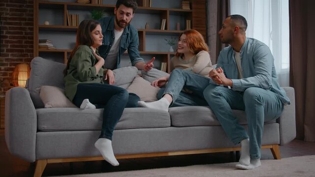 Happy four multiethnic friends at home party on couch talking carefree group of multiracial diversity people men women laughing having fun together discussing at apartment meeting chatting friendly