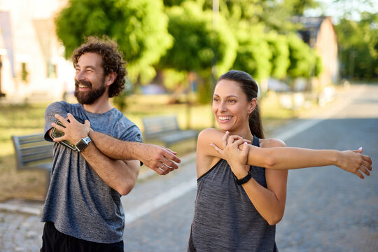 Two individuals engage in stretching exercises in a park during the morning. They appear relaxed and joyful while focusing on their warm-up routine.