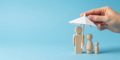 Family Life Insurance Coverage Concept: Hand protecting wooden people figures with paper umbrella on blue background wide banner