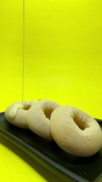 Unglazed doughnuts on a black tray being dipped in condensed milk against a vibrant yellow background - Vertical video