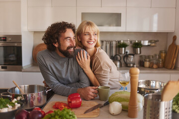 Two people are happily cooking in a stylish kitchen filled with fresh ingredients. They are smiling and enjoying each other's company while getting ready for a meal.