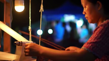 Skilled artisan weaving traditional fabric by hand under warm light at a night market. - Powered by Adobe