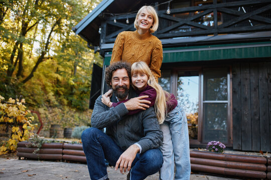 A happy family enjoys their time together outdoors in autumn. They are smiling and posing outside their home surrounded by vibrant fall colors.