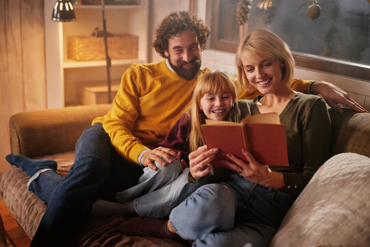 A family enjoys reading a book together on a comfortable sofa in their cozy living room during the evening. The warm atmosphere enhances their shared moment.