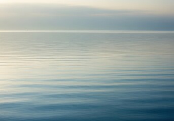 Serene and tranquil expanse of calm water reflecting the soft, muted light of a peaceful sky at dawn or dusk