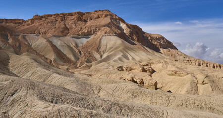 Majestic panoramic landscape in Mazok Hazinim nature reserve in the Negev Desert. Close up view of orange sandstone hills and mountain folds. White clouds on blue sky. Less travelled hiking trails