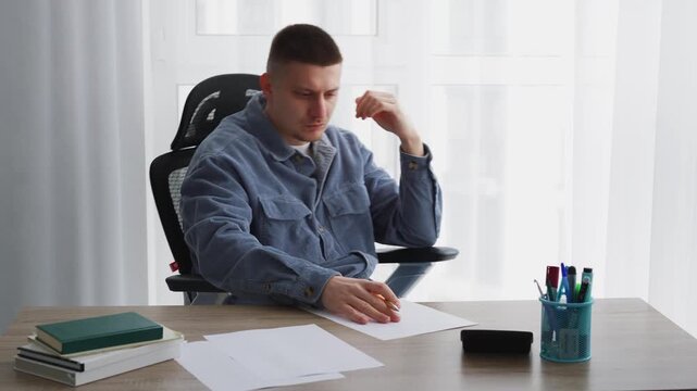 A man sits at a desk, writing something with a pen on a white sheet of paper.
A screenwriter writes a text on a piece of paper.
Education and training, a smart guy writes something with a pen.
Writing