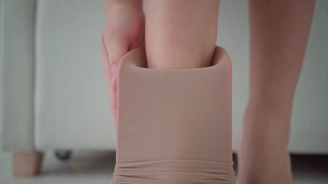 A woman places her foot into a compression stocking held on an assist device, showing a close view of the fabric and the first step of putting it on.