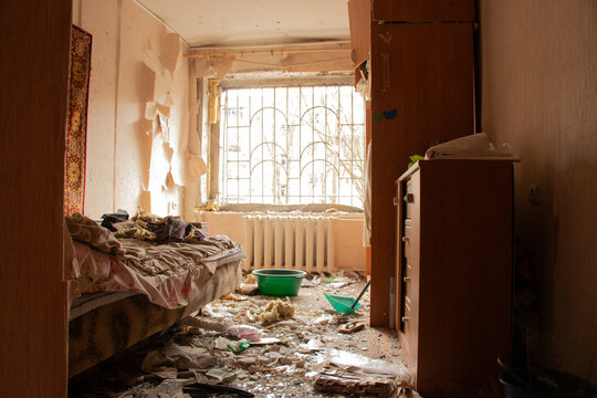 A destroyed apartment after a drone explosion under the window of a multi-story building, with broken windows and spilled belongings and traces of destruction during the war