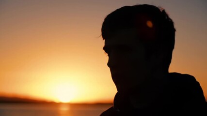Silhouette of person against warm sunset sky over water, with head facing right