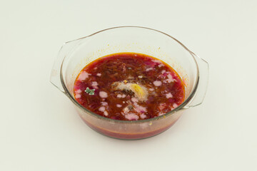 A glass bowl of spoiled red borscht is shown from an angle on a light background, with visible mold spots forming across the surface of the soup.