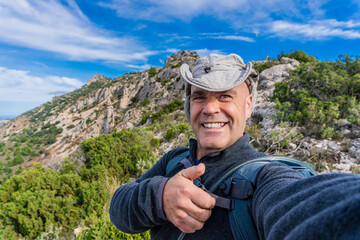Hiker taking a selfie with thumbs up, outdoors.