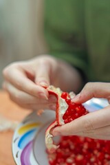 Girl peeling pomegranate and extracting juicy red seeds for healthy eating