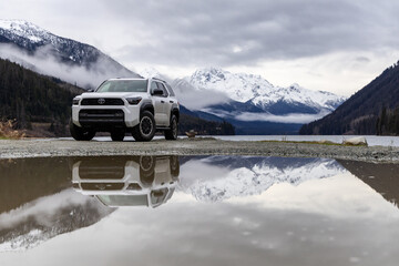 Naklejka premium White Toyota 4Runner SUV By Mountain Lake With Reflections, Snowy Peaks, And Overcast Sky