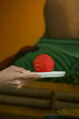 Close-up of a hand holding a white plate with a raspberry shaped red dessert.