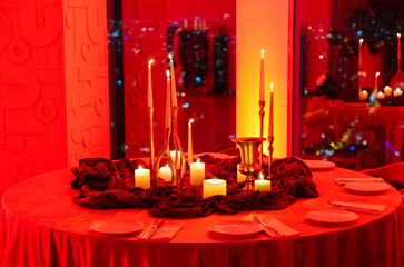A romantic dinner table set with candles, red lighting, and elegant decor, creating an intimate atmosphere. The soft glow from the candles and warm lighting sets the mood for a special evening