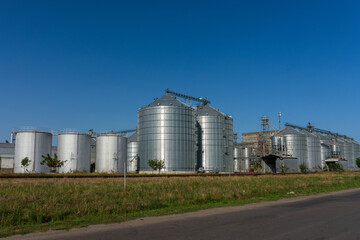 Grain silos stand tall under the clear blue sky on a sunny day in a rural industrial area