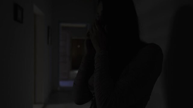 Girlfriend taking a secret phone call in a dark hallway, whispering so her partner wont hear, hidden affair