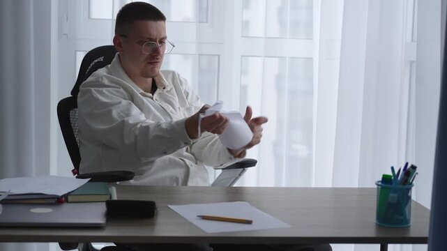 A man in a white shirt reads documents and tears them up while sitting in an office.
An angry man at work tears up a sheet of paper and can't control his emotions.
Paper, tearing, fatigue, nerves, emo