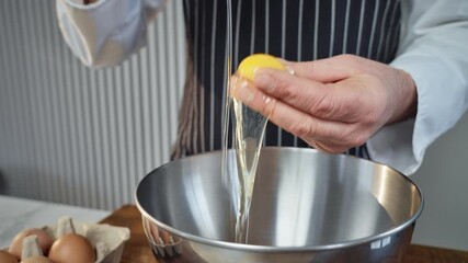 skilled baker in striped apron carefully cracking eggs into mixing bowl in professional kitchen - Powered by Adobe