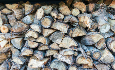 A detailed view of freshly cut firewood stacked tightly in an orderly pile. The rough tree rings, bark textures, and natural tones highlight warmth, craftsmanship, and rustic outdoor living.