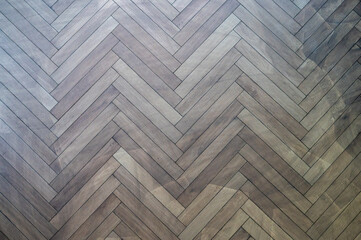 Herringbone wood flooring pattern with natural grain texture in neutral brown tones.