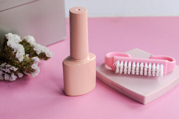 Pink nail polish bottle and a manicure brush with white bristles on a pastel pink background, symbolizing self care, beauty, and wellness treatment for healthy fingernails