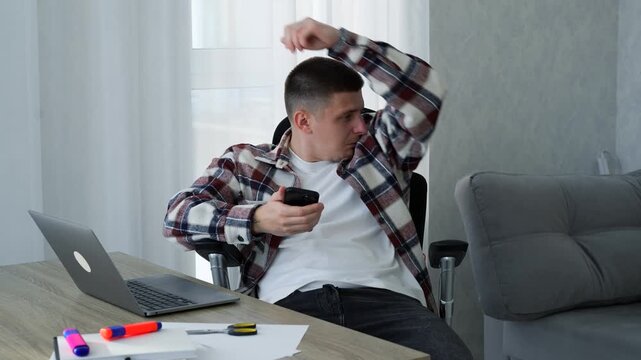 A man's armpits are sweaty and he has an unpleasant odor.
A foul-smelling man sits in an office chair and sniffs his armpits.
Poor hygiene and grooming.