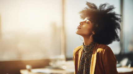 A Woman with afro hair pauses, basking in sunlight near the window. She closes her eyes, in a reflective pose, appearing calm and at peace during her break