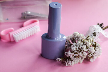 Pastel lilac nail polish bottle on a pink background, featuring a nail brush, manicure toolkit, and delicate dried flowers for a self care beauty routine