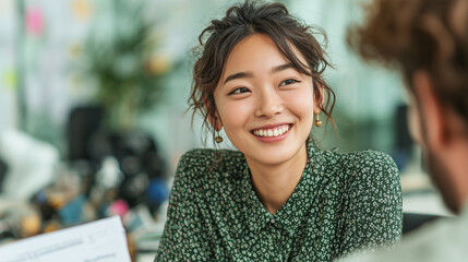 Female employer (Asian) interviewing male candidate (Caucasian), friendly expressions, modern bright office, documents on desk