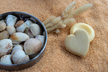 Spa and wellness elements including natural heart shaped soap, bath towel, dried grass, and a bowl of seashells, creating a serene environment for self care and relaxation