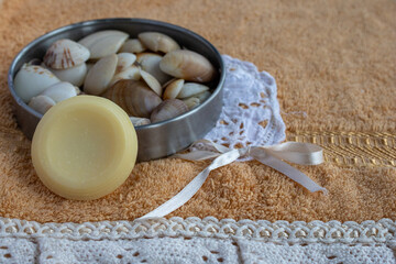 Relaxing spa scene with natural soap bar, sea shells in a metal bowl, and a delicate white lace ribbon on a soft orange towel, creating a sense of tranquility and self care