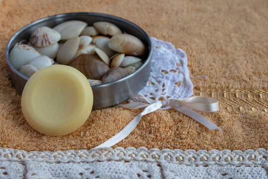 Relaxing spa scene with natural soap bar, sea shells in a metal bowl, and a delicate white lace ribbon on a soft orange towel, creating a sense of tranquility and self care - Powered by Adobe