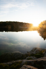 Idyllic landcsape in sweden with a calm lake reflecting the surrounding forest , a rocky...