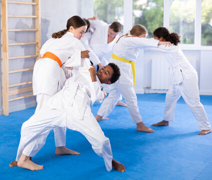 Focused teenage girl in martial arts uniform practicing fighting techniques during sparring with african american boy