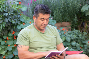 Hombre de 60 a&ntilde;os con ropa deportiva leyendo una libreta de apuntes rodeado de un jard&iacute;n verde