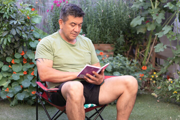 Hombre de 60 a&ntilde;os con ropa deportiva leyendo una libreta de apuntes rodeado de un jard&iacute;n verde