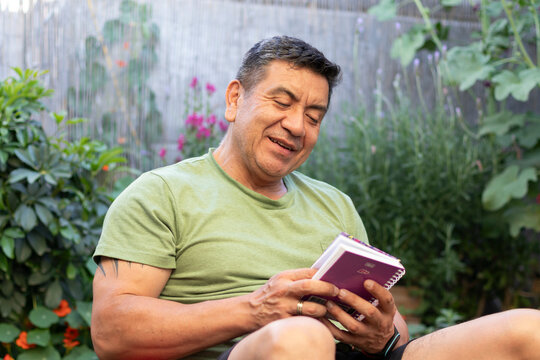 Hombre de 60 a&ntilde;os con ropa deportiva leyendo una libreta de apuntes rodeado de un jard&iacute;n verde