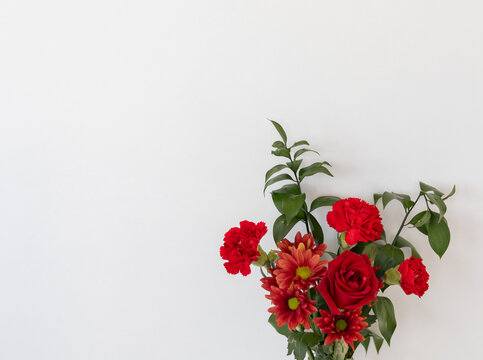 A bouquet of red flowers, including roses and chrysanthemums, arranged in a clear glass vase. The composition highlights the vivid colors, natural textures, and elegance of the floral arrangement.
