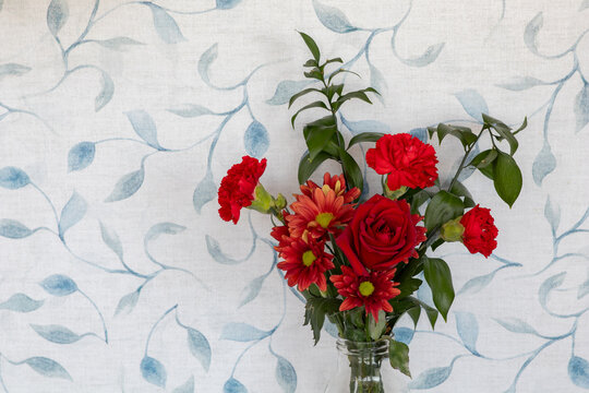 A bouquet of red flowers, including roses and chrysanthemums, arranged in a clear glass vase. The composition highlights the vivid colors, natural textures, and elegance of the floral arrangement.