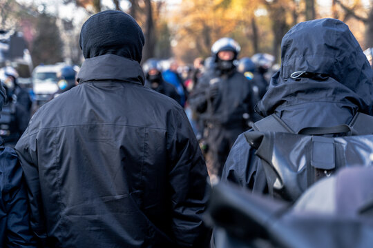 Anonymous masked left wing antifa, or so called black block is standing in front of a riot police line with helmets on in Germany to block other protesters.