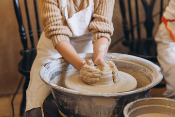 Child hands creating pottery on spinning wheel