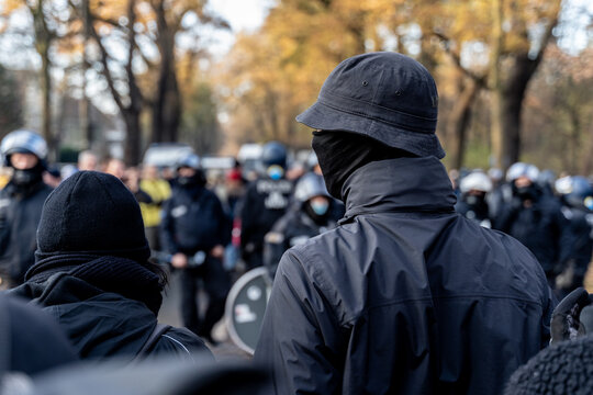 Anonymous masked left wing antifa, or so called black block is standing in front of a riot police line with helmets on in Germany to block other protesters.